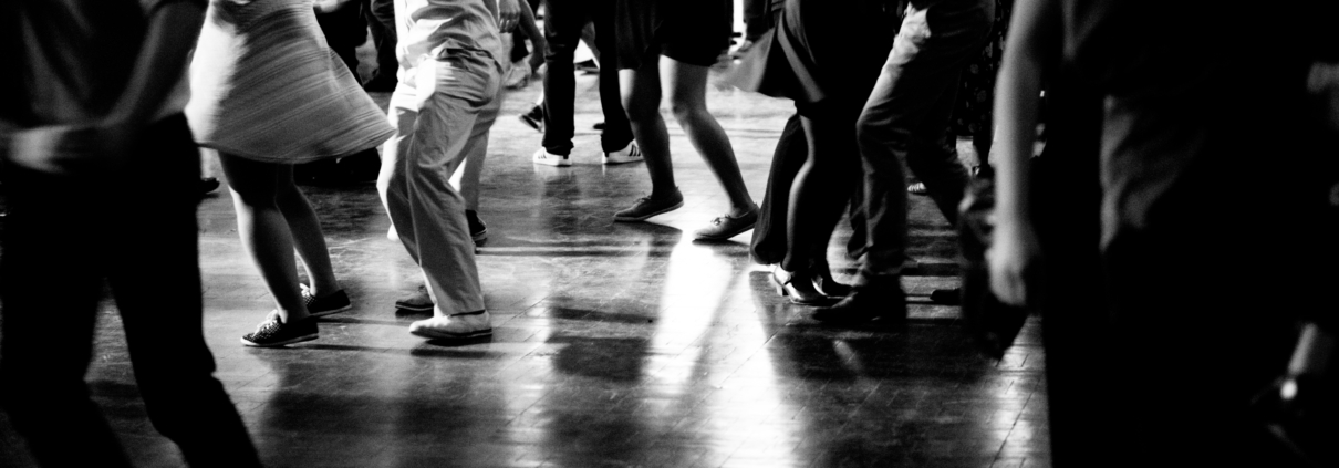 Black and white below shoulder view of many people dancing